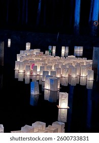 Illuminated floating lanterns create a serene and peaceful atmosphere on a calm water surface at night, reflecting a soft light against the dark surroundings of a river.
