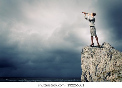 Image of businesswoman looking in telescope standing atop of rock