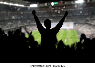 Image of a full stadium with silhouettes of fan on the foreground