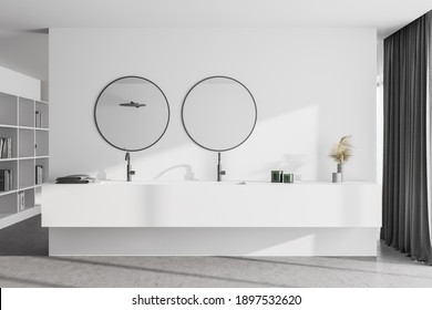 Interior of modern bathroom with white walls, concrete floor and double sink with round mirrors. Bookcase in the background. 3d rendering