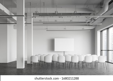 Interior Of Modern Industrial Style Office Lecture Hall With White Walls, Concrete Floor, Rows Of White Chairs And Mock Up Projection Screen. Concept Of Presentation And Education. 3d Rendering