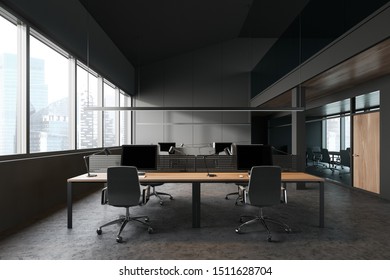 Interior Of Modern Office With Dark Gray Walls, Concrete Floor, Large Window With Cityscape, Rows Of Wooden Computer Tables And Meeting Room To The Right. 3d Rendering