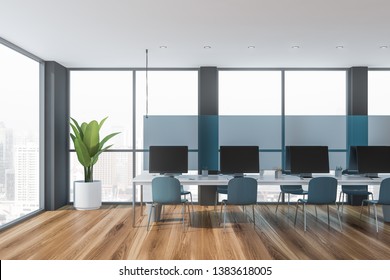 Interior Of Modern Open Space Office With Large Windows, Wooden Floor, Long White Table With Row Of Computers And Bright Blue Chairs. Blue Glass Separation Panel. 3d Rendering