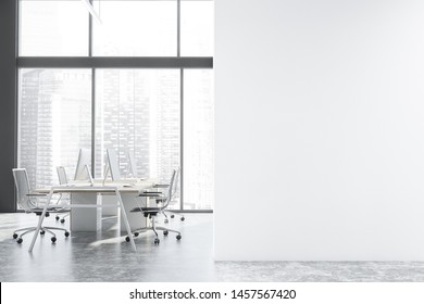 Interior Of Panoramic Open Space Office With Gray Walls, Concrete Floor, Large Windows With Cityscape And Rows Of White And Wooden Computer Tables. Mock Up Wall To The Right. 3d Rendering