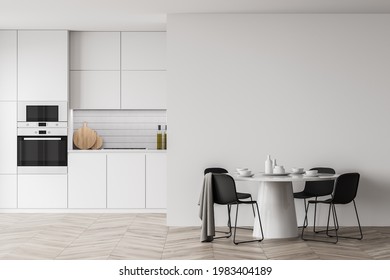 Interior Of Trendy White Kitchen Featuring Cabinets, Built In Sink And Cooker And Cupboards Hanging Above Them. Round Dining Table. Blurry Cityscape. Concept Of Cooking And Home. 3d Rendering Mock Up