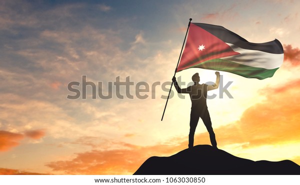 Jordan flag being waved by a man\
celebrating success at the top of a mountain. 3D\
Rendering