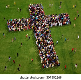 Large group of people seen from above gathered together in the shape of  a cross, on a grass background