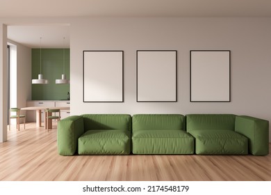 Light kitchen interior with lounge zone, sofa and dining table with chairs on hardwood floor. Chill and cooking area in modern apartment. Three mockup posters in row. 3D rendering