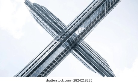 A low angle perspective of two modern glass skyscrapers intersecting against a bright white sky, creating a geometric X shape.