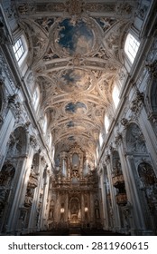 A low-angle view of the ornate, vaulted ceiling and interior of a historic European cathedral featuring intricate baroque frescoes and architectural details.