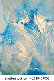 Luxury abstract fluid art painting in alcohol ink technique, mixture of blue and gold paints.  Imitation of marble stone cut, glowing golden veins. Tender and dreamy design. 