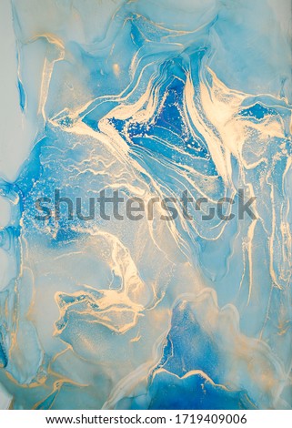 Luxury abstract fluid art painting in alcohol ink technique, mixture of blue and gold paints.  Imitation of marble stone cut, glowing golden veins. Tender and dreamy design. 