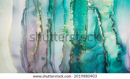 Luxury abstract painting in fluid art technique.Transparent vertical layers of green, blue, purple and gold paints create marbled texture of stripes, swirls and veins with glowing gold and glitter.