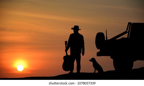 Man hold the guitar he is watching The sun is falling Beside the car and dog