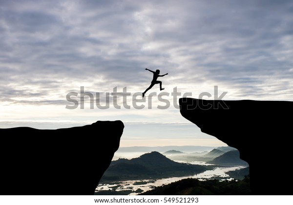 Man jump through the gap\
between hill.man jumping over cliff on sunset background,Business\
concept idea
