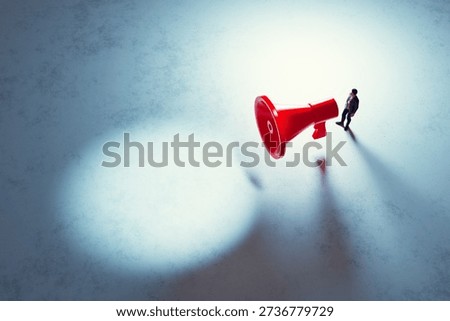Man standing next to large red funnel or megaphone in spotlight. Important message.