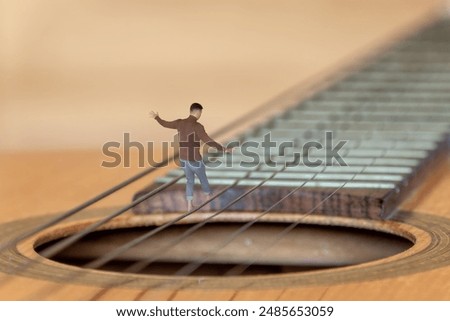 A man walks on the string of a giant guitar over the guitar's socket, as if over an abyss. An illustration on the risk of failure in a musical career.