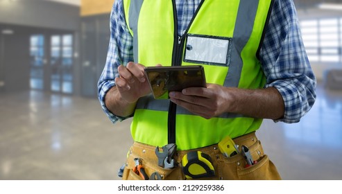 Midsection of male caucasian construction worker wearing reflective clothing using digital tablet. unaltered, blue-collar worker, skilled, industry and technology concept. - Powered by Shutterstock