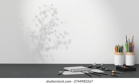 Minimal creative desk setup with art supplies, notebooks, pencils, and a vase with flowers against a clean wall background. Modern workspace scene with copy space for branding and design projects.