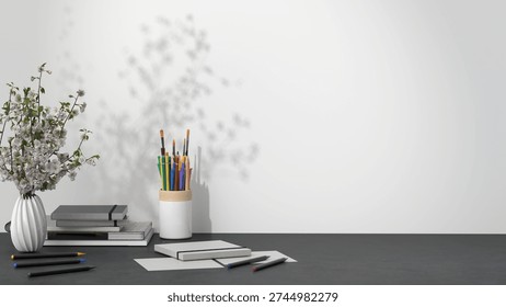 Minimal creative desk setup with art supplies, notebooks, pencils, and a vase with flowers against a clean wall background. Modern workspace scene with copy space for branding and design projects.