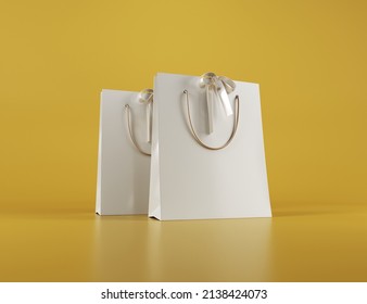 Mockup Of White Paper Bag On Yellow Background. Two Bags With Gold Handles. Satin Ribbons. Eco Package With Space For A Logo. Place For Text. Shopping Package. 3D Illustration.