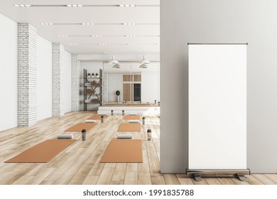 Modern Concrete Yoga Gym Interior With Equipment, Blank Poster On Wall, Daylight And Wooden Flooring. Healthy Lifestyle Concept. Mock Up, 3D Rendering