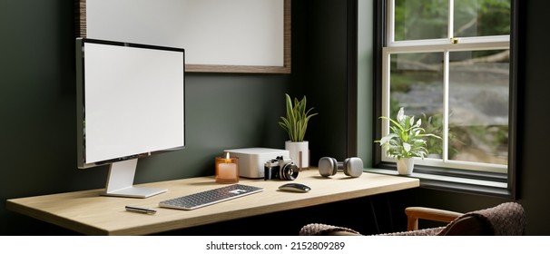 Modern Contemporary Home Office Workspace With Pc Desktop Computer Mockup, Camera, Headphone, Keyboard And Accessories On Table Over Dark Green Wall With Frame Mockup. 3d Rendering, 3d Illustration