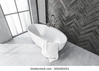 Modern grey bathroom interior with an oval white ceramic bathtub, a metallic towel rack and tiled floor with the dark parquet style wall. Corner view. A concept of trendy design. 3d rendering