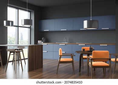 Modern Grey And Blue Modular Kitchen Cabinet With Steel Details, Dark Wood Floor, Bar Table And Orange Chairs In Dining Area. Concept Of Kitchen Space Interior Design. Corner View. 3d Rendering