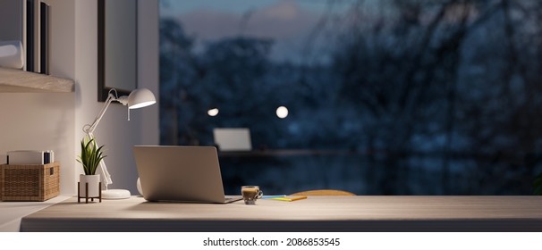Modern home office room with laptop computer and copy space on working desk over blurred outdoor view at night in the background. 3d rendering, 3d illustration