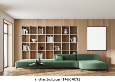 Modern living room interior with large green sofa, white empty poster on the wooden wall, built-in bookshelf, window. Concept of home library. Contemporary minimalist design. Mock up. 3d rendering