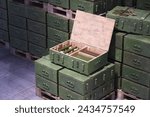 A neatly arranged collection of green military ammunition boxes on wooden pallets, with one container open, showcasing a variety of shells and bullets in a secure depot setting.