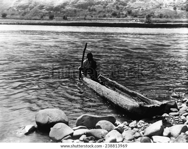 Nez Perc_ canoe.\
Nez Perc_ man with pole maneuvering dugout canoe to rocky shore.\
Edward S. Curtis, ca.\
1910