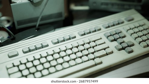 An old computer keyboard sits on a cluttered desk surrounded by various items. The keyboard shows signs of wear, indicating extensive use over time and capturing a nostalgic vibe.