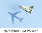 Paper plane made of a US 100 dollar bill flying over a blue sea background and projecting a realistic commercial flight shadow. 3D illustration of the concept of travel budget and air ticket prices