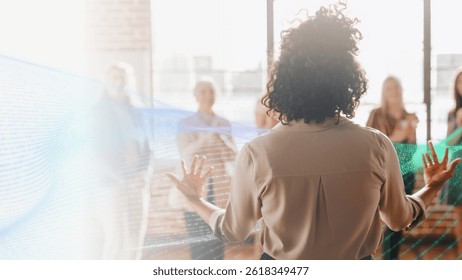 A person with curly hair speaks to a group in a bright room. They face the audience, engaging in a presentation or discussion with attentive listeners. Technology image.