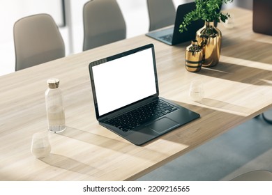 Perspective View On Modern Black Laptop With Blank White Screen With Space For Your Logo Or Text On Wooden Table With Glass Of Water And Golden Vases In Sunlit Office. 3D Rendering, Mock Up