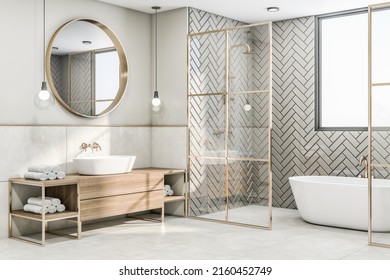 Perspective view on sunny modern interior design bathroom with herringbone ceramic tales bath zone, wooden sink cabinet under round mirror and glass partitions with gold decorations. 3D rendering - Powered by Shutterstock