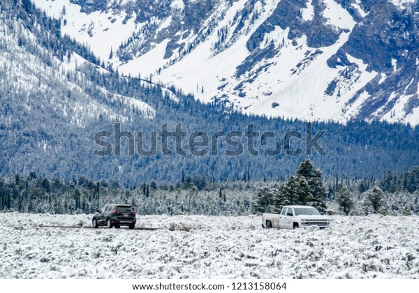 Pickup truck and sport utility vehicle travel in\
opposite directions in Grand Teton National Park, Wyoming, USA, on\
a snowy day, with digital oil-painting effect, for themes of travel\
and tourism