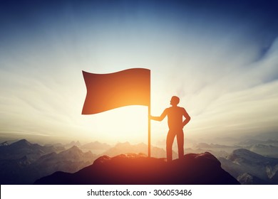 Proud man raising a flag on the peak of the mountain. Successful challenge concept, new achievement