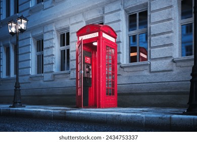 A quintessentially British red telephone booth casts a warm glow on a cobblestone street under the evening sky, embodying the timeless charm of the United Kingdom's urban scenery.