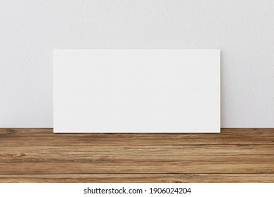 Rectangular blank canvas of 2x1 proportions on wooden surface and white wall to present artwork, illustrations or photos. 3D Rendering