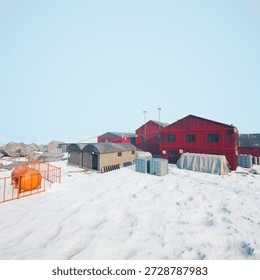 Red and gray structures stand amidst a vast snowy terrain, accompanied by storage containers and equipment.
