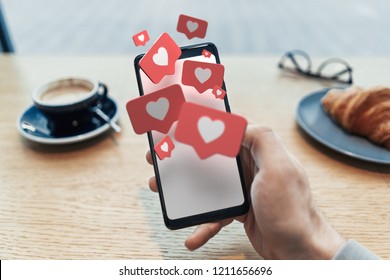 Red heart Like symbols on blank mobile phone screen. Close up of man hand holding mobile phone in cafe. 3d rendering. Social media concept.