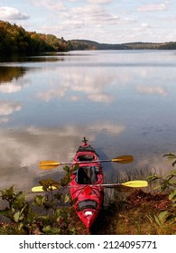 Red kayak resting on the shore of a hilly forest lake with clouds reflected in clear water. Phillip lake landscape Quebec 