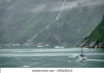 Sailor standing near bow of sailboat approaches a steep rock formation above glacial ice floes on tidewaters of Tracy Arm fjord in southeastern Alaska, USA, with digital oil-painting effect