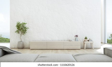 Sea View Living Room Of Luxury Summer Beach House With TV Stand And Wooden Cabinet. Empty Rough White Concrete Wall Background In Vacation Home Or Holiday Villa. Hotel Interior 3d Illustration.