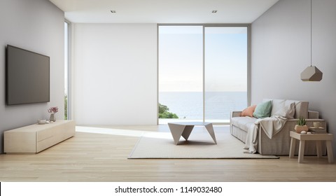 Sea view living room of luxury beach house with glass door and wooden terrace. TV on gray wall against white sofa in vacation home or holiday villa. Hotel interior 3d illustration.