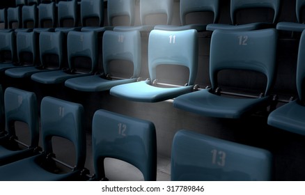 A section of numbered stadium seating set in rows coin the dark with one seat  being singled out by a spotlight 