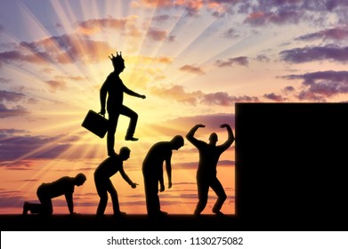 A Selfish Man With A Crown On His Head, Walking On The Heads Of People As On The Steps To The Top. Conceptual Scene Of A Narcissistic And Selfish Businessman